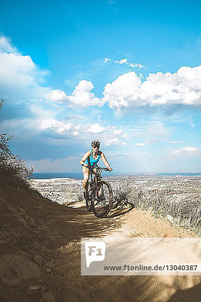 Female cyclist riding mountain bike on arid landscape against cloudy sky