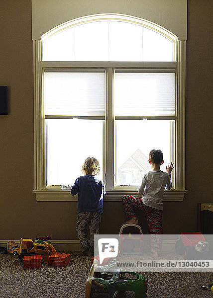 Rückansicht von Jungen  die zu Hause durch das Fenster schauen