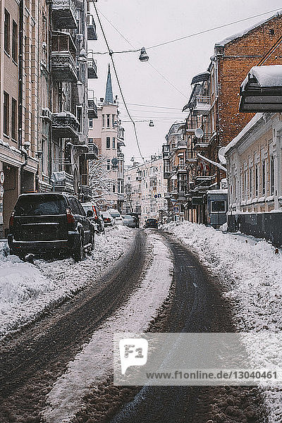 Autos parken auf schneebedeckter Straße inmitten von Gebäuden in der Stadt