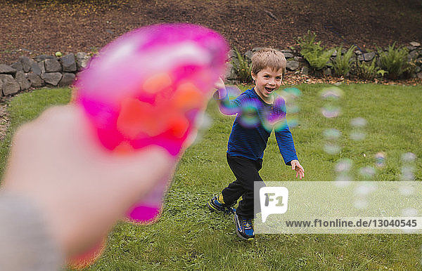 Ausgeschnittenes Bild einer Hand  die eine Blasenpistole hält  während sie mit einem Jungen im Hof spielt