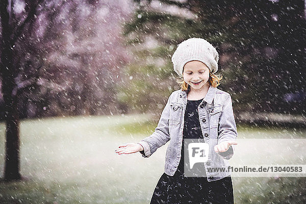 Lächelndes Mädchen steht bei Schneefall im Park