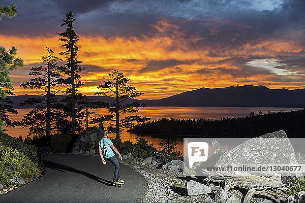 Mann fährt Skateboard auf Fußweg am See gegen dramatischen Himmel
