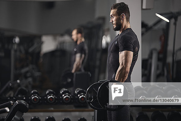 Seitenansicht eines Mannes  der eine Hantel hebt  während er im Fitnessstudio trainiert