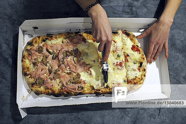 Abgehackte Hände einer Frau  die zu Hause auf der Küchentheke Pizza schneidet