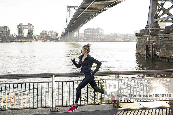 Side view of confident athlete running on promenade by East River