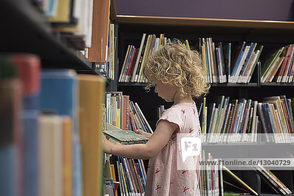 Side view of girl looking at book while standing in library