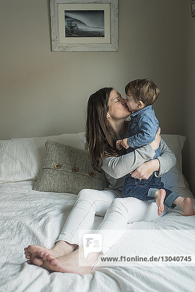 Mother embracing while kissing son on bed at home