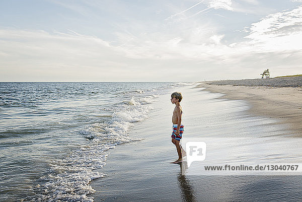 Seitenansicht eines Jungen ohne Hemd  der weg schaut  während er am Tobay Beach gegen den Himmel steht