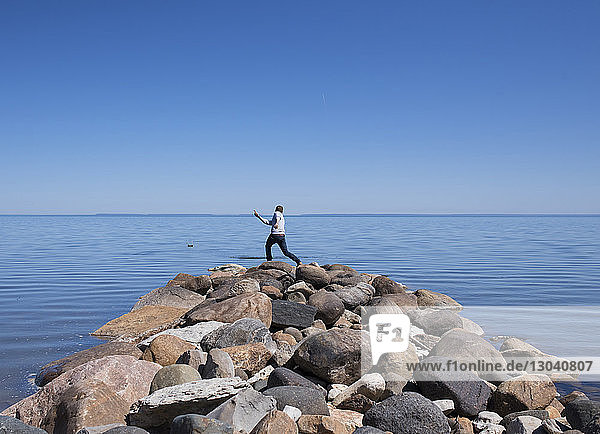 Rear view of man standing on rocky beach against clear blue sky