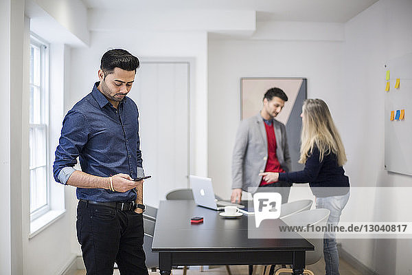 Businessman using smart phone with colleagues standing at desk in background
