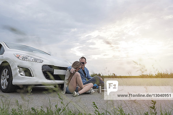 Glückliches Paar sitzt mit dem Auto auf der Landstraße vor bewölktem Himmel