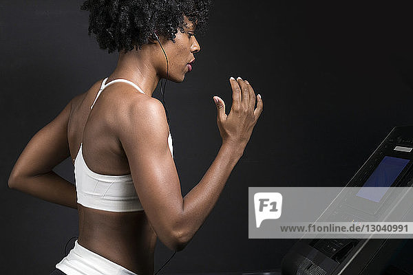 Seitenansicht einer Frau  die auf einem Laufband läuft  während sie im Fitnessstudio an der Wand Musik hört