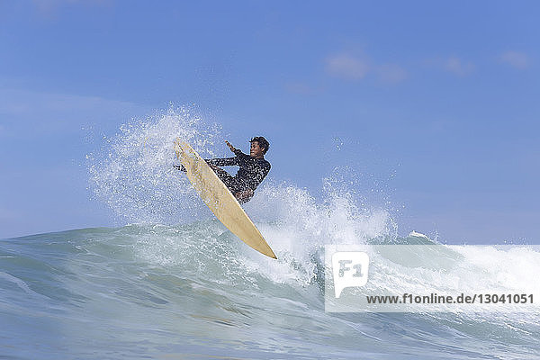 Man surfing on sea against blue sky