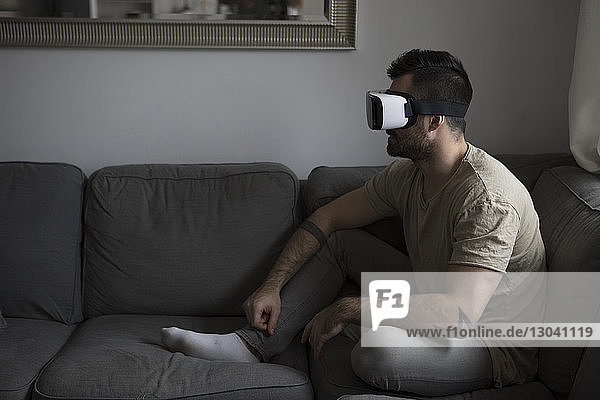 Man using virtual reality simulator while sitting sofa at home
