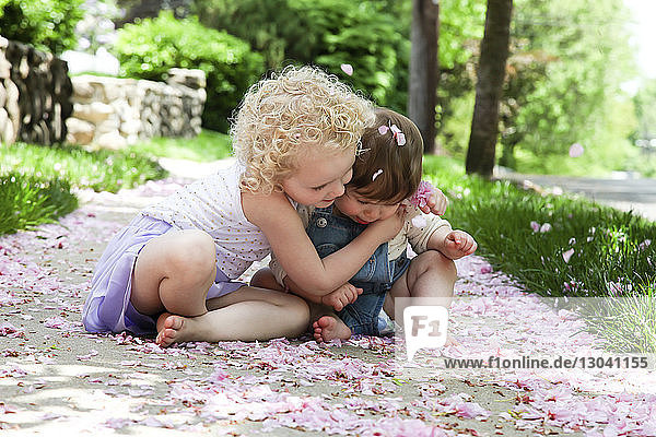 Mädchen umarmt Schwester  während sie auf einem Fußweg im Park sitzt