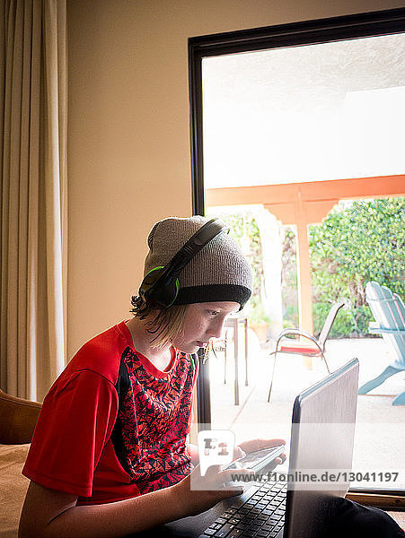 Junge schaut auf Laptop-Computer  während er zu Hause ein Smartphone benutzt