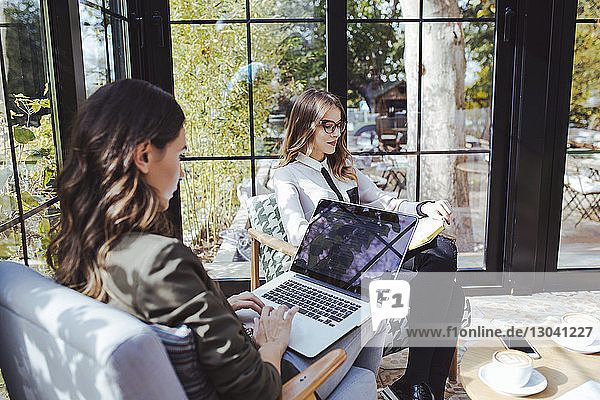 Frau benutzt Laptop-Computer  während ein Kollege im Café ein Buch liest