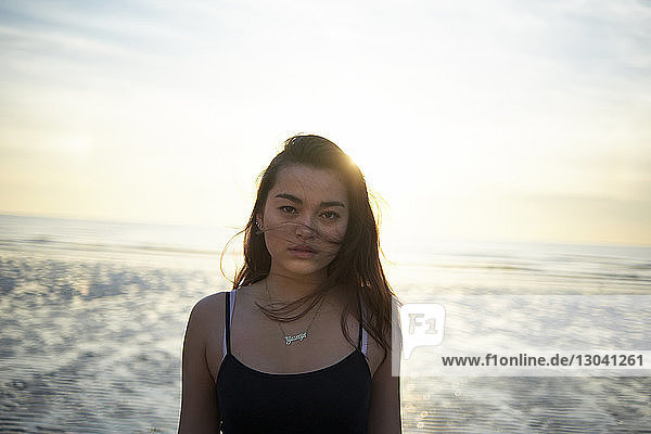 Porträt einer selbstbewussten Teenagerin  die bei Sonnenuntergang am Strand steht
