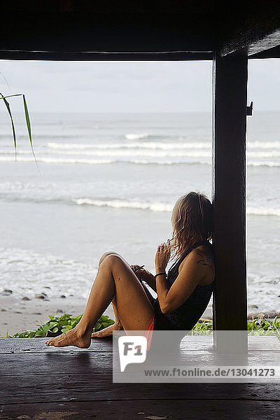 Seitenansicht einer Frau  die auf einer Diele am Strand sitzt