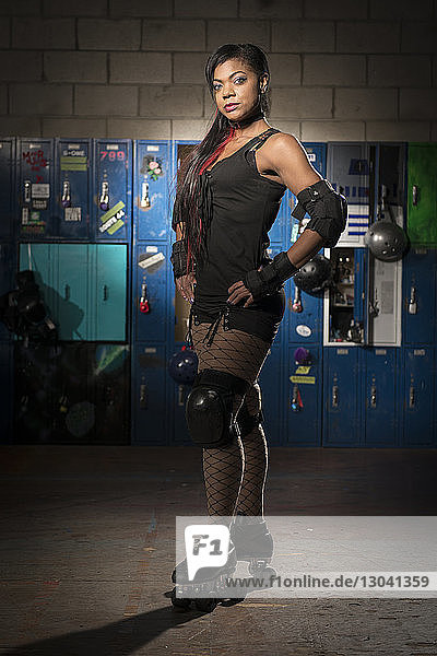 Portrait of confident sportswoman with hands on hip wearing roller skates while standing against lockers