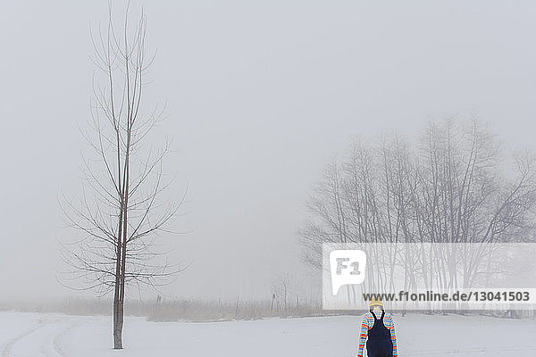 Rear view of girl walking on snow covered field in forest during foggy weather