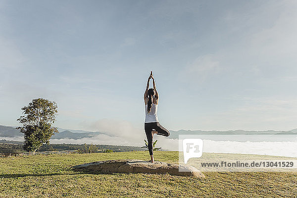 Rückansicht einer Frau beim Yoga auf einem Grasfeld gegen den Himmel
