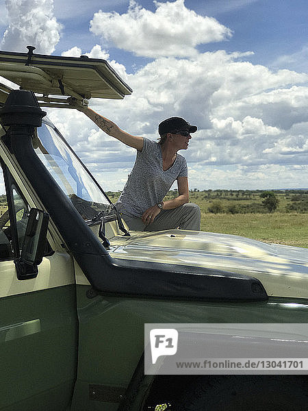 Tourist standing by off-road vehicle against cloudy sky during safari