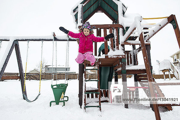 Verspieltes Mädchen springt im Winter auf dem Spielplatz von Spielgeräten im Freien
