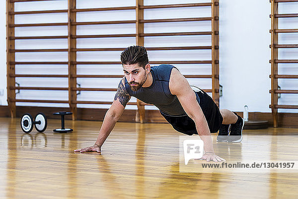 Muskulöser Athlet in voller Länge beim Liegestützen auf Hartholzboden im Fitnessstudio