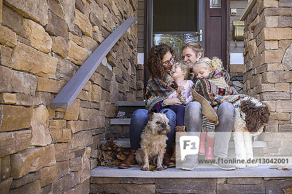 Glückliche Familie in eine Decke gehüllt mit Hunden  die auf Stufen vor dem Haus sitzen