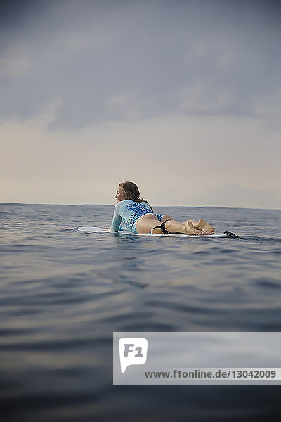 Sorglose Frau in voller Länge auf einem Surfbrett im Meer gegen den Himmel liegend