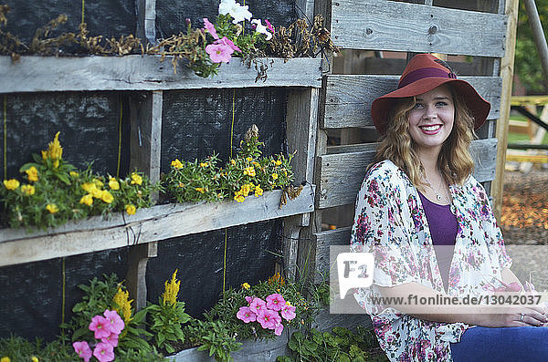 Porträt einer lächelnden Frau  die an blühenden Pflanzen im Gemeinschaftsgarten sitzt