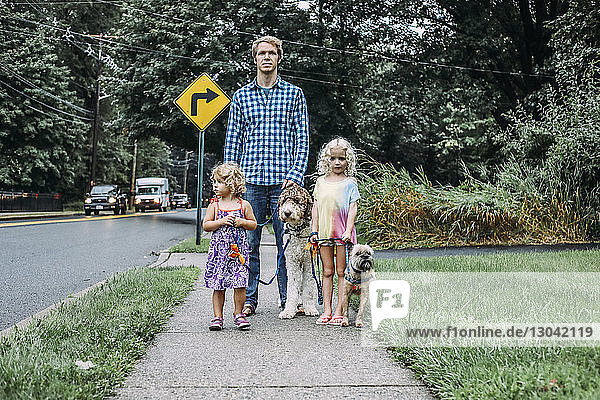 Vater und Töchter stehen mit Hunden auf dem Gehweg auf dem Rasen