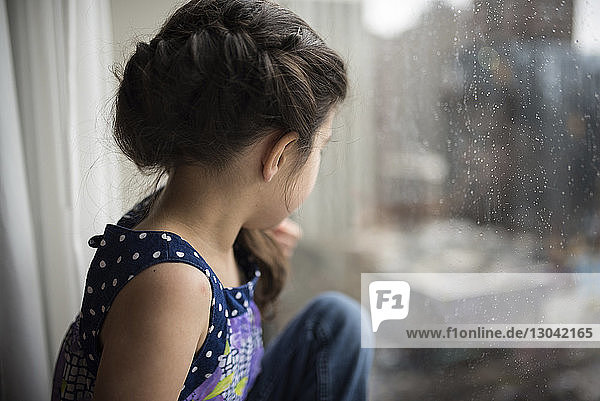 Nachdenkliches Mädchen schaut durch ein nasses Fenster zu Hause