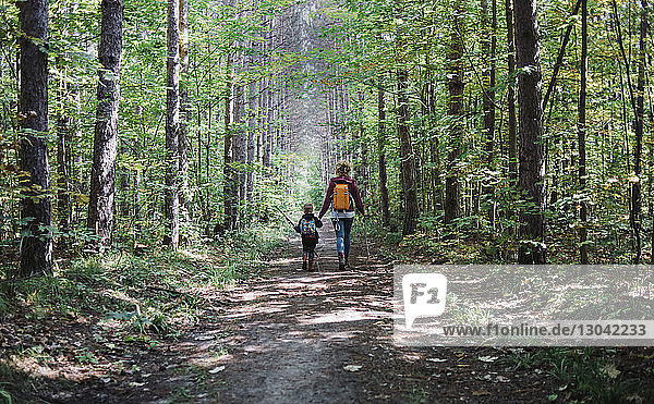 Rear view of mother and son with backpack hiking in forest
