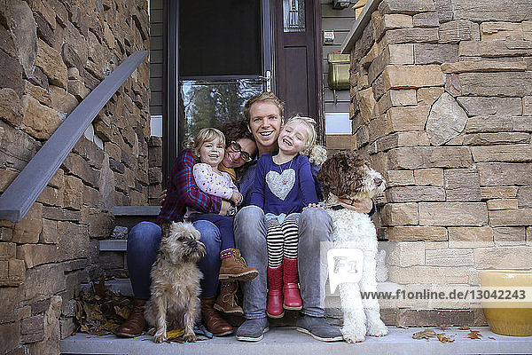 Porträt einer glücklichen Familie mit Hunden  die auf Stufen vor dem Haus sitzen