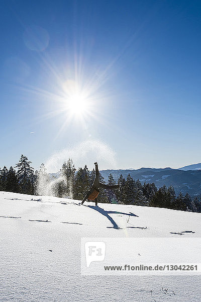 Mann dreht bei Sonnenschein auf verschneitem Feld gegen den Himmel