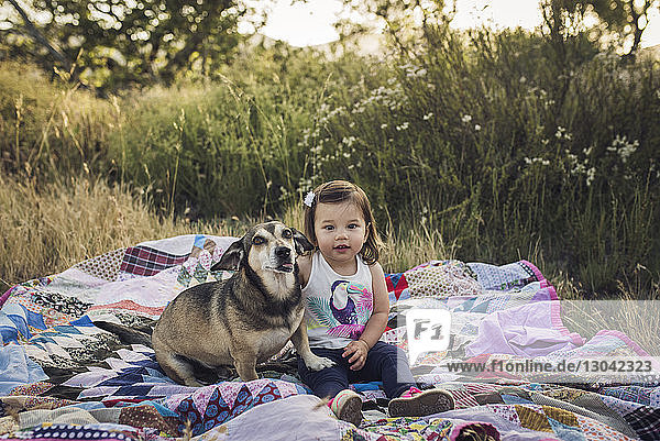 Portrait of girl and dog sitting on picnic blanket at field