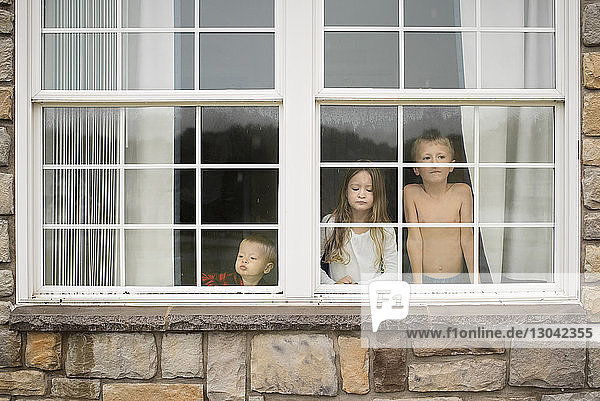 Geschwister schauen zu Hause durchs Fenster