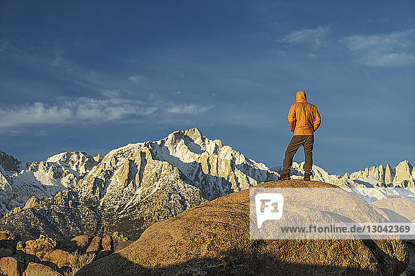 Rear view of man in warm clothing standing on mountain against sky during sunset