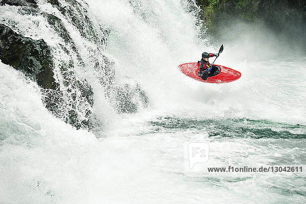 Whitewater kayaker paddling through river in forest