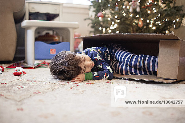 Boy sleeping in cardboard box at home during Christmas