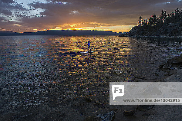 Mann paddelt bei Sonnenuntergang auf dem See