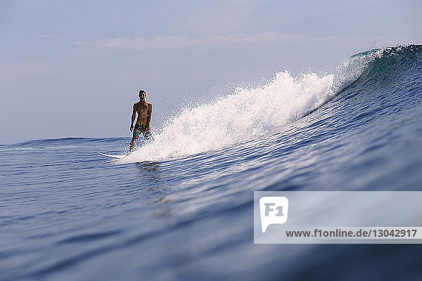Mann schreit  während er auf einer Welle im Meer surft