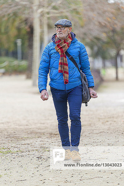 Man in warm clothing looking away while walking on field at park
