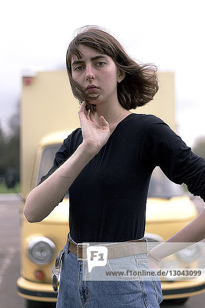 Porträt einer selbstbewussten jungen Frau mit der Hand in der Gesäßtasche  die gegen einen Lastwagen steht