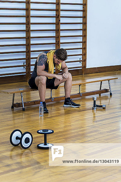 Athlet in voller Länge auf Bank sitzend im Fitnessstudio