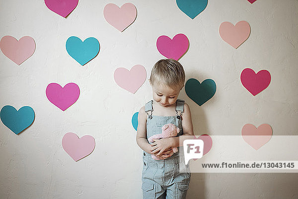 Junge steht mit ausgestopftem Spielzeug an der mit Herzformen verzierten Wand zu Hause