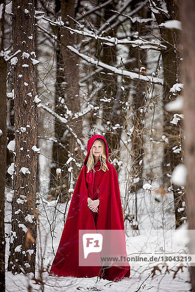 Portrait of girl wearing red dress while standing on snow covered field