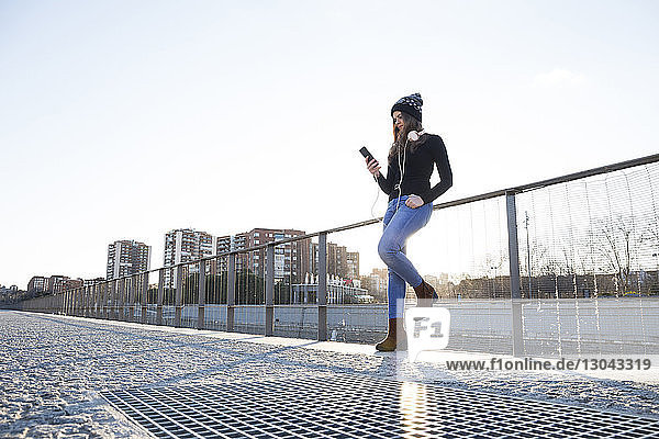 Niedrigwinkelansicht einer Frau  die ein Mobiltelefon benutzt  während sie in der Stadt am Geländer steht